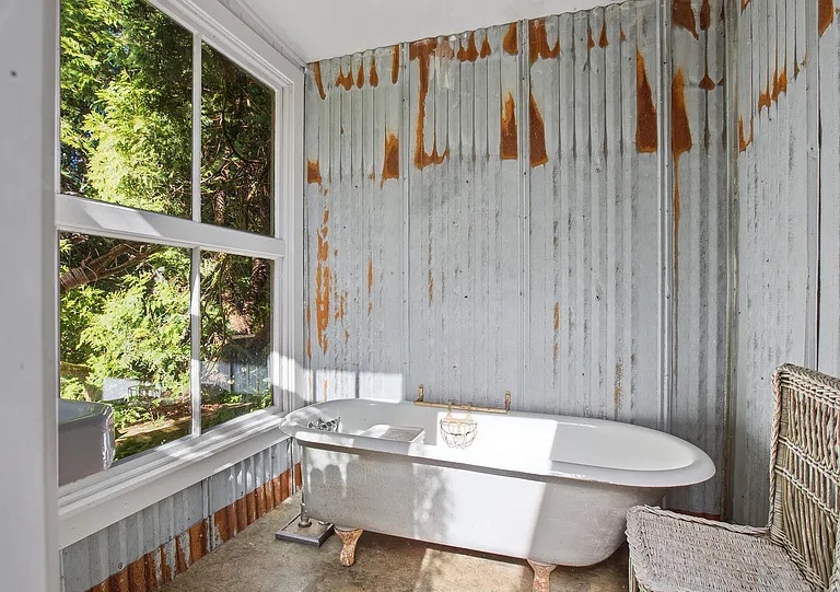 Claw-foot soaking tub set in a window-lined bathing room overlooking the trees