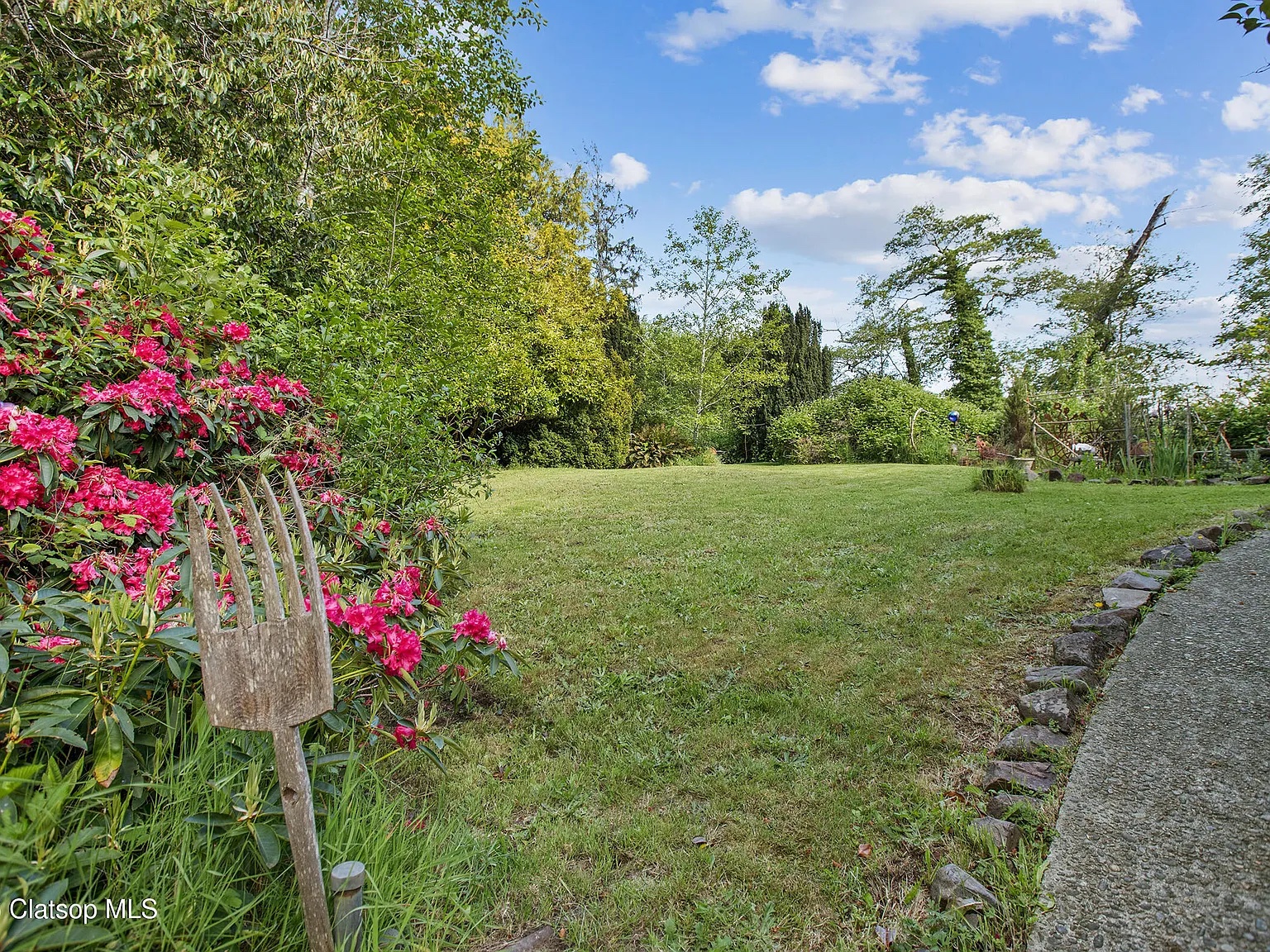 Wide green lawn bordered by rhododendrons and mature trees